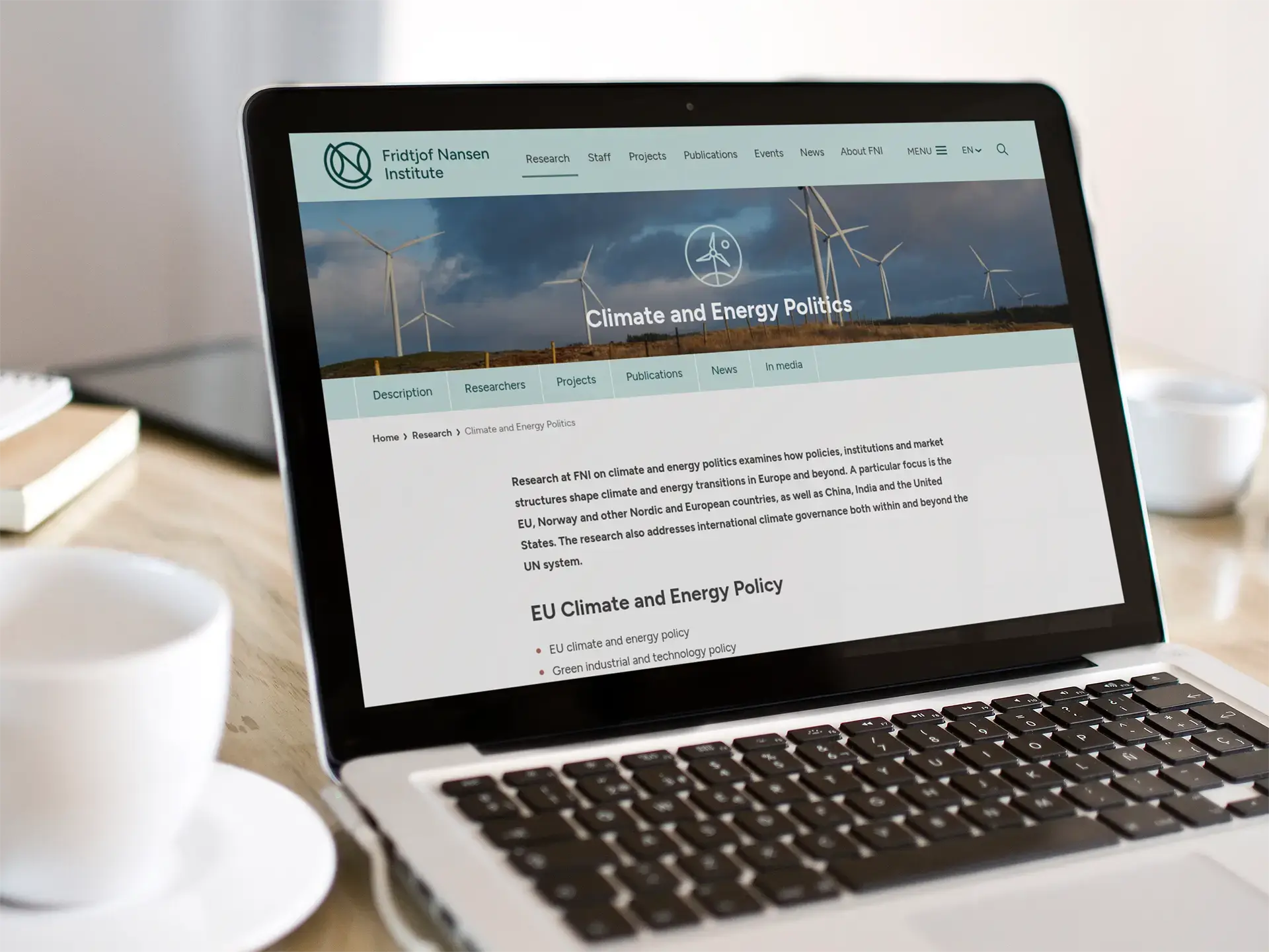 Laptop åpen på fnis nettside omringet av kaffekopp og notatblokker